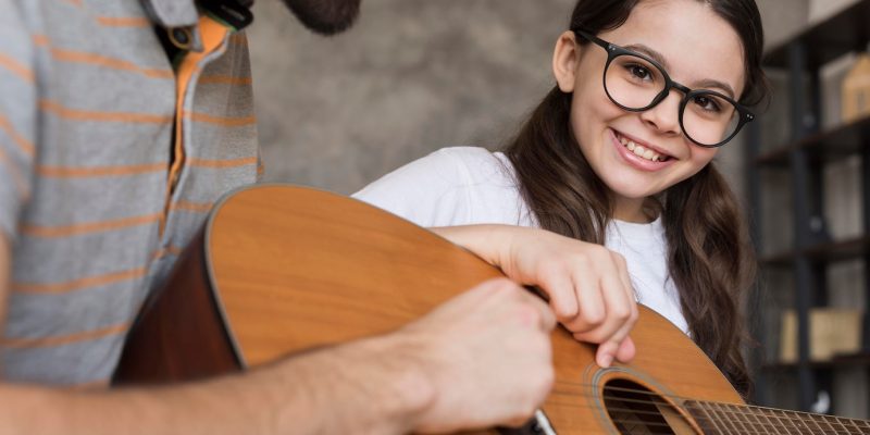 close-up-papa-ensenando-nina-tocar-guitarra_23-2148542815