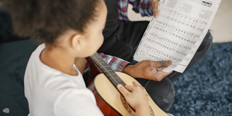padre-con-hija-en-el-sofa-chica-sosteniendo-una-guitarra-aprendiendo-tocar-la-guitarra (1)