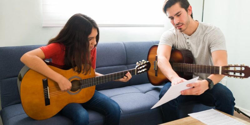 sigue-la-partitura-profesor-de-musica-hispana-hablando-con-un-estudiante-sobre-tocar-una-cancion-en-la-guitarra-acustica-durante-las-lecciones-en-casa (1) sigue-la-partitura-profesor-de-musica-hispana-hablando-con-un-estudiante-sobre-tocar-una-cancion-en-la-guitarra-acustica-durante-las-lecciones-en-casa (1)